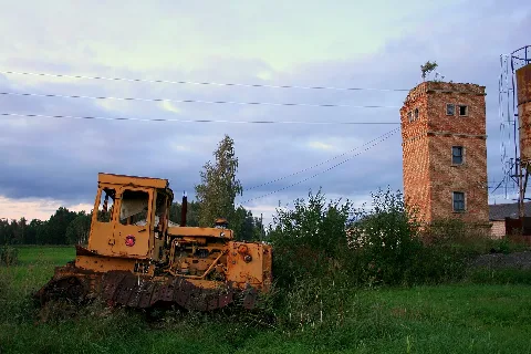 Abandoned Yellow Caterpillar Tractor And Water Tower In Skrunda Fish Farm